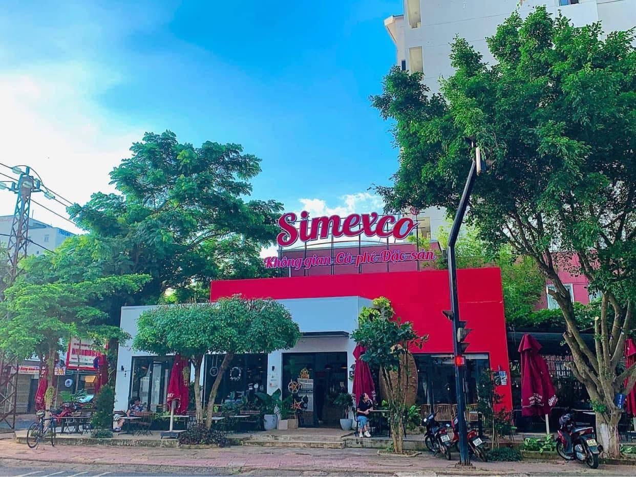 Mặt tiền quán ban ngày: tòa nhà sơn đỏ, biển Simexco, hàng cây xanh phía trước