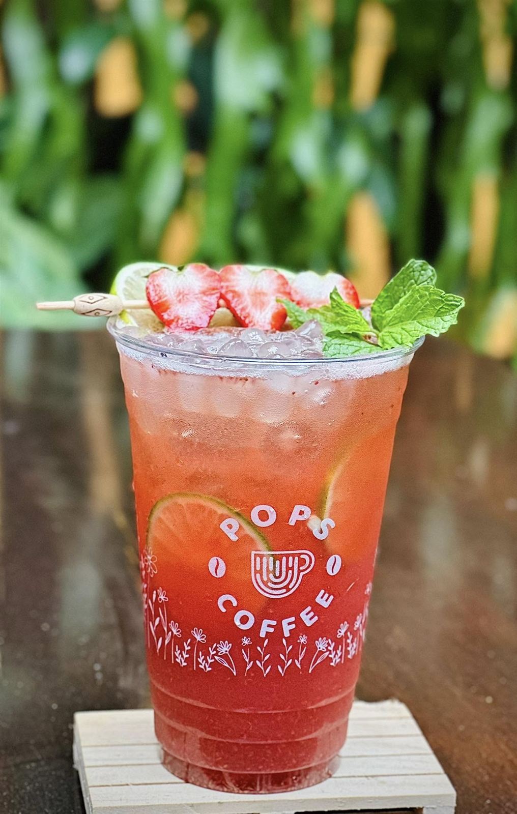 Ly nước trái cây màu đỏ trong cốc in logo POPS Coffee, trang trí dâu và lá bạc hà